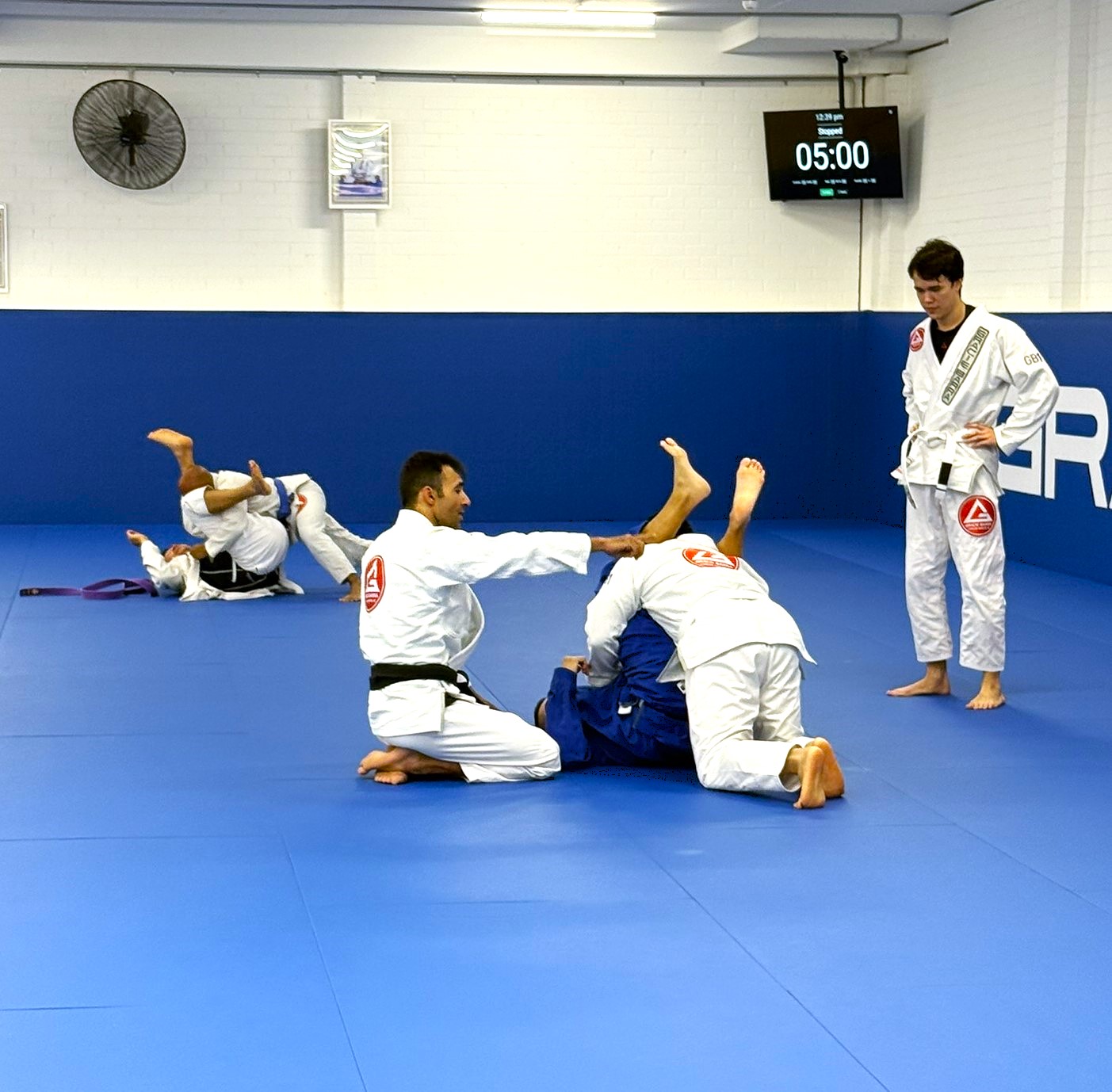 Coach assisting beginners in a BJJ fundamentals class at Gracie Barra Artarmon