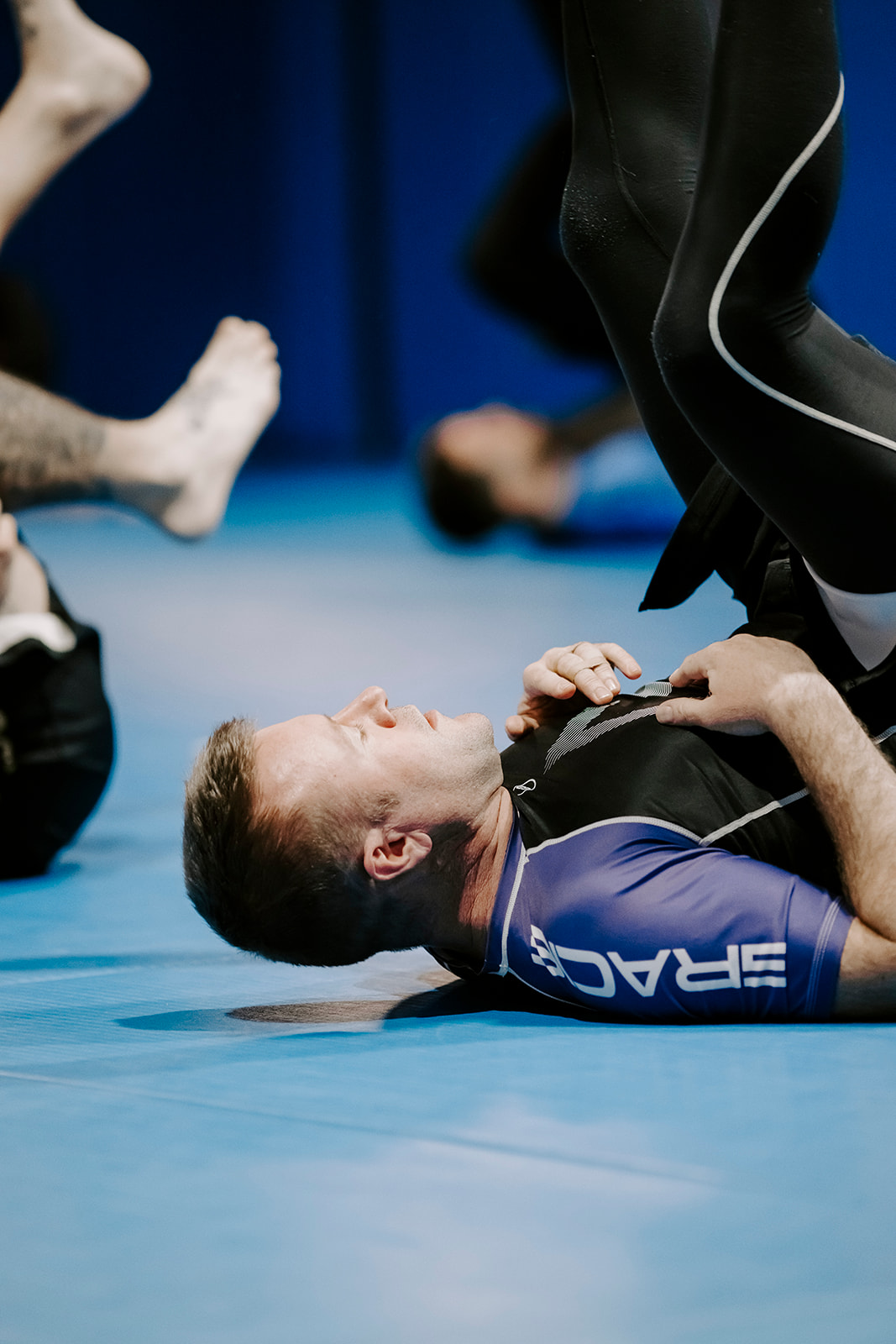 Man wearing a purple-rank rash guard performing warm-up exercises during an advanced Brazilian Jiu-Jitsu class.