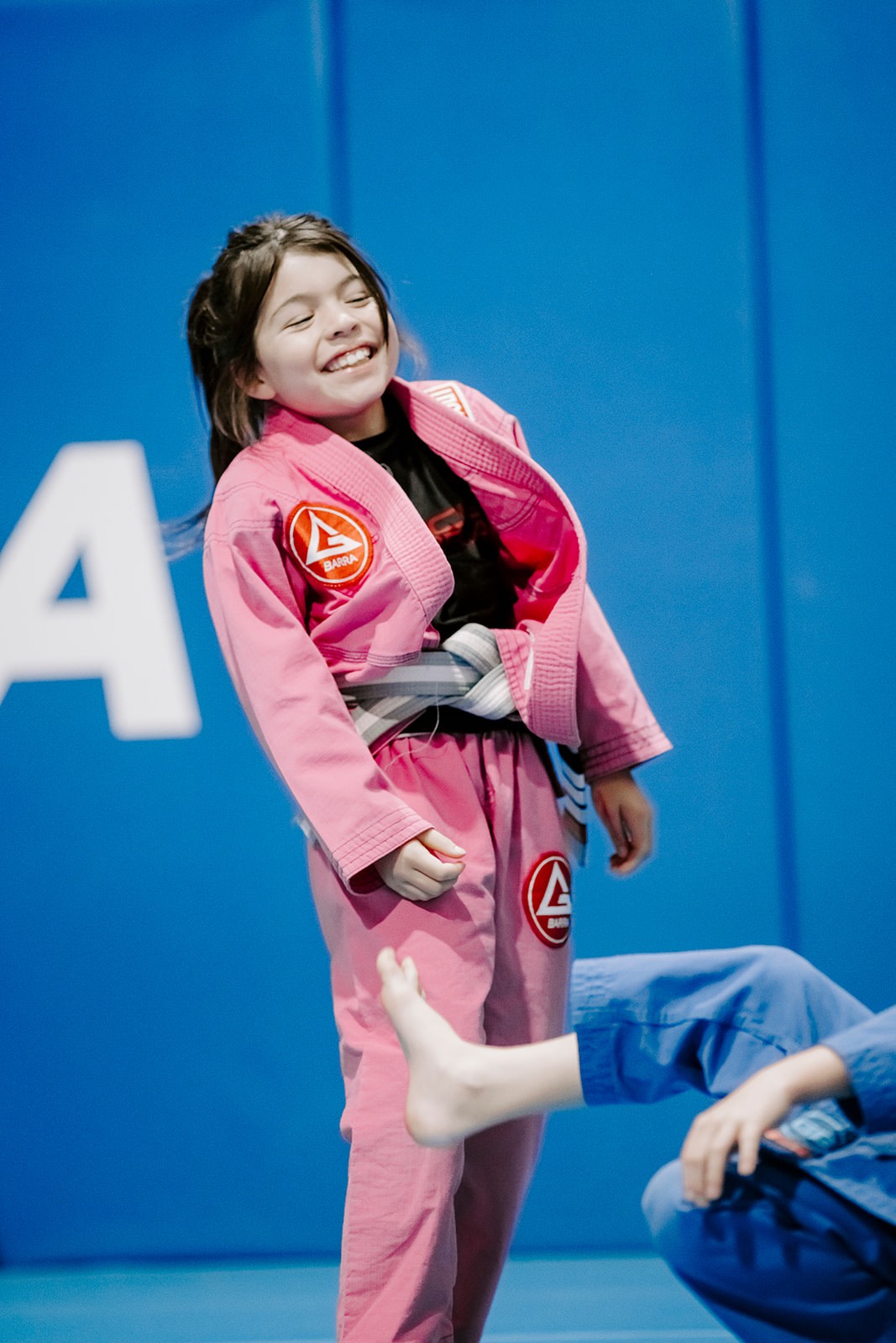 9-year-old girl laughing and having fun on the BJJ mat in a pink gi.